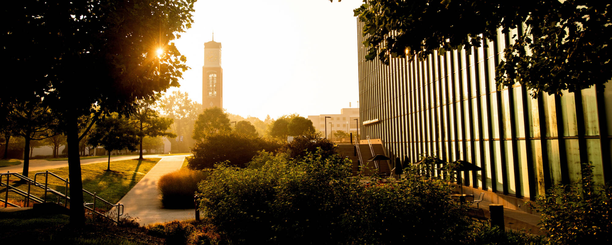 The Mary Idema Pew Library windows reflect the sunrise with the Cook Carillon clock tower in the distance.